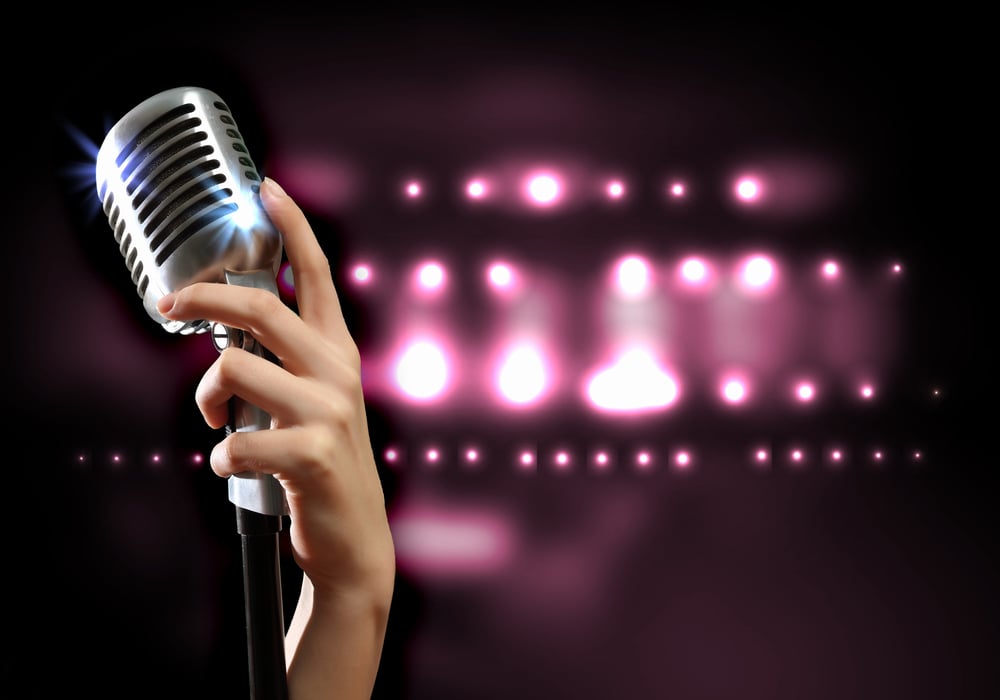 Female hand holding a single retro microphone against colourful background